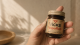 Hand holding a jar of Vicks VapoRub against a neutral background